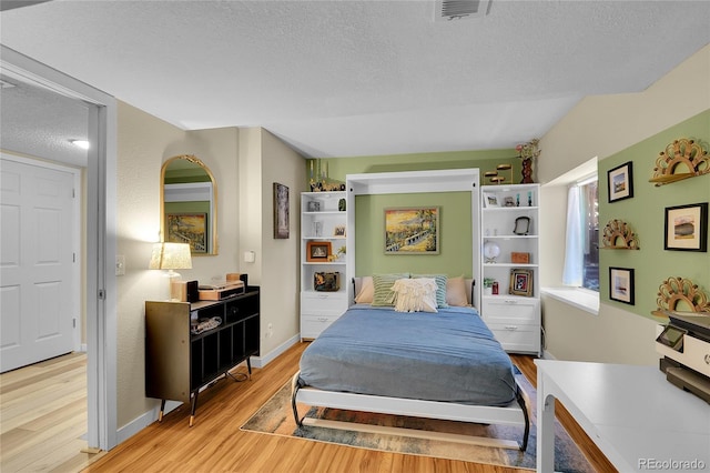 bedroom featuring light wood-type flooring, a textured ceiling, and baseboards