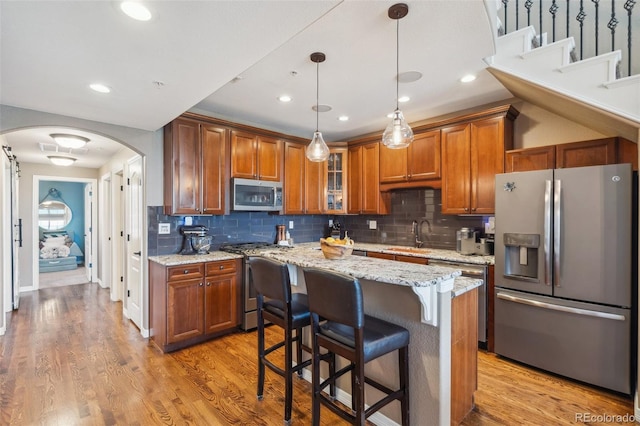 248 Writers Way, Colorado Springs, CO 80903 - kitchen with appliances with stainless steel finishes, brown cabinetry, arched walkways, a kitchen breakfast bar, and backsplash