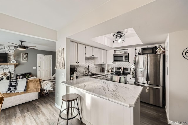 kitchen with white cabinets, stainless steel appliances, decorative backsplash, sink, and kitchen peninsula