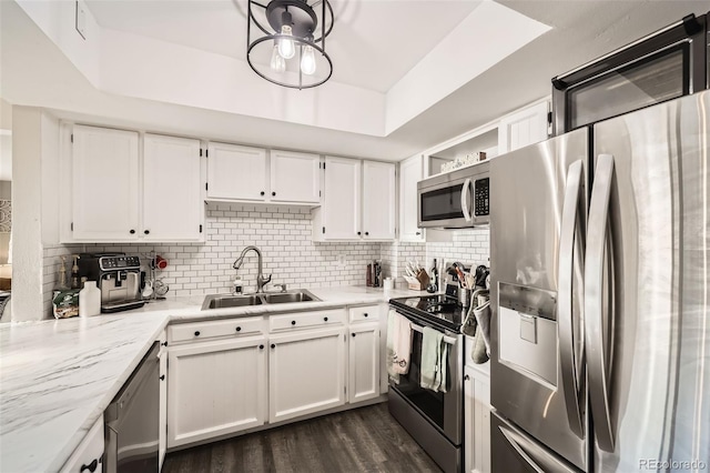 kitchen with sink, a tray ceiling, white cabinetry, appliances with stainless steel finishes, and light stone counters