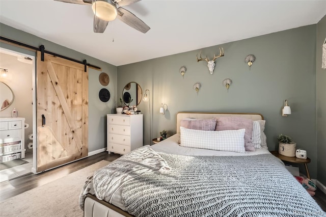 bedroom with ceiling fan, a barn door, dark wood-type flooring, and ensuite bathroom