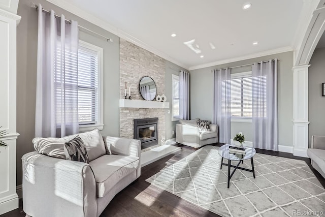 living room featuring a stone fireplace, a healthy amount of sunlight, ornate columns, and crown molding