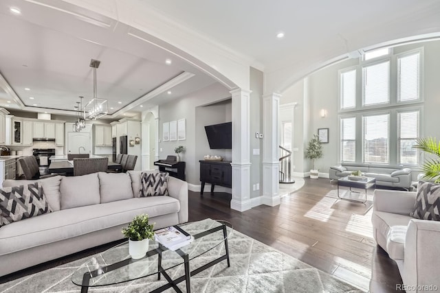 living room featuring sink, ornate columns, dark wood-type flooring, and crown molding