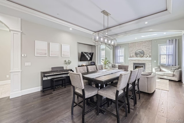 dining area featuring ornamental molding, decorative columns, dark wood-type flooring, and a raised ceiling