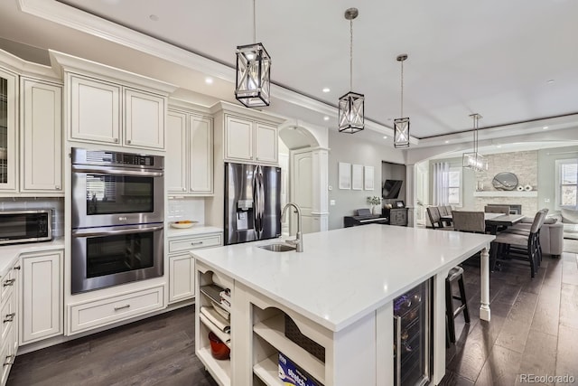 kitchen with pendant lighting, sink, an island with sink, beverage cooler, and stainless steel appliances