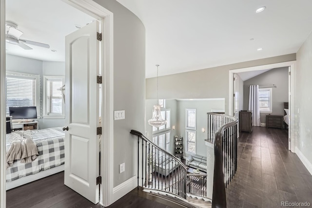 corridor featuring plenty of natural light, dark hardwood / wood-style floors, a notable chandelier, and vaulted ceiling