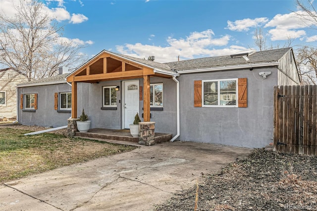 bungalow-style home featuring stucco siding, roof with shingles, and fence