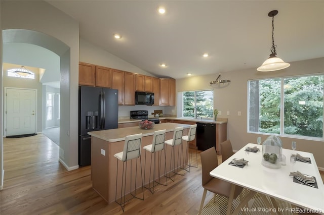 kitchen featuring vaulted ceiling, decorative light fixtures, a kitchen island, black appliances, and light wood-type flooring