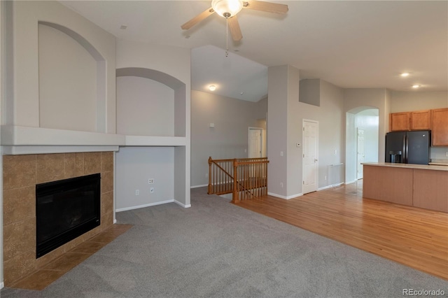 unfurnished living room with ceiling fan, light carpet, high vaulted ceiling, and a tiled fireplace