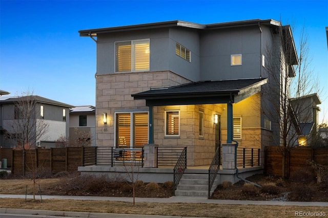 contemporary home featuring stone siding, fence, and covered porch