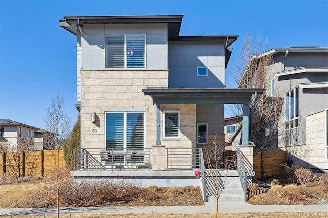 view of front of property with covered porch, stone siding, and fence