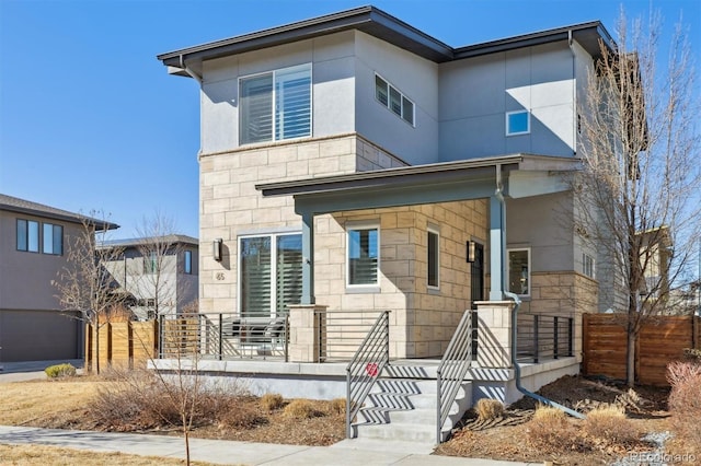 modern home with covered porch, stone siding, and fence