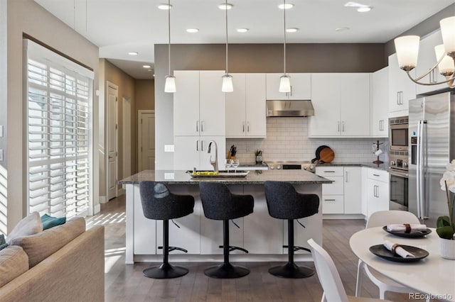 kitchen featuring stainless steel appliances, a breakfast bar, dark wood finished floors, and under cabinet range hood