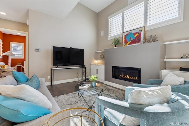 living room with a glass covered fireplace, plenty of natural light, wood finished floors, and baseboards