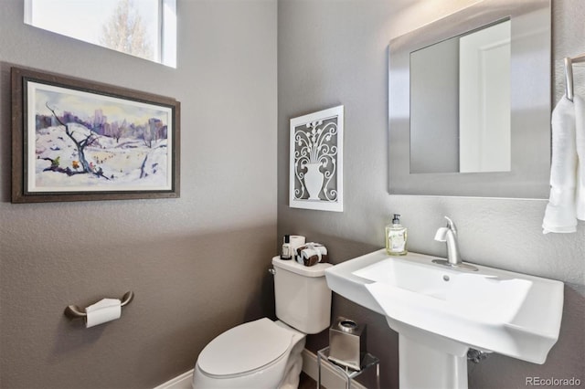 half bathroom featuring toilet, a sink, and a textured wall