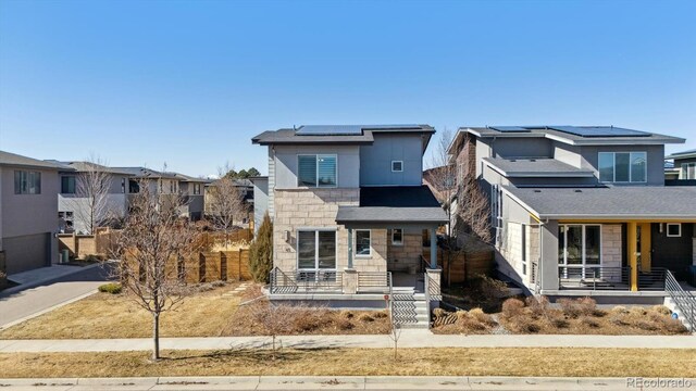 view of front of home featuring covered porch, stone siding, fence, and solar panels