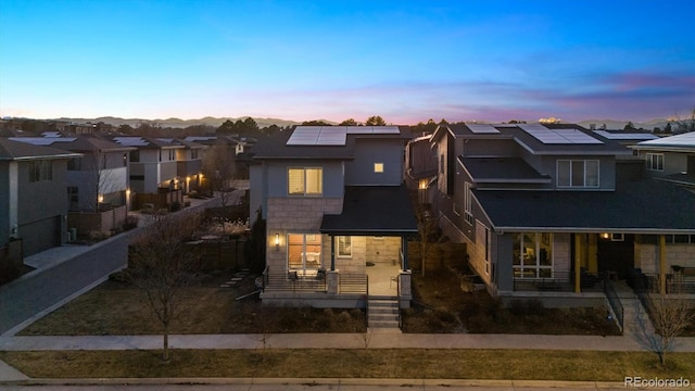 view of front of house with stone siding, a residential view, covered porch, and roof mounted solar panels