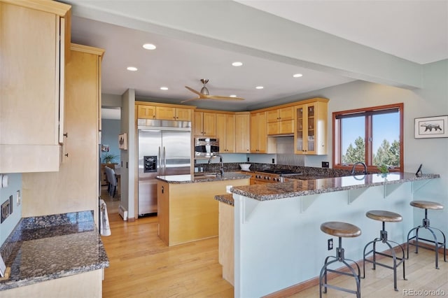 kitchen featuring kitchen peninsula, a kitchen breakfast bar, dark stone counters, stainless steel appliances, and ceiling fan