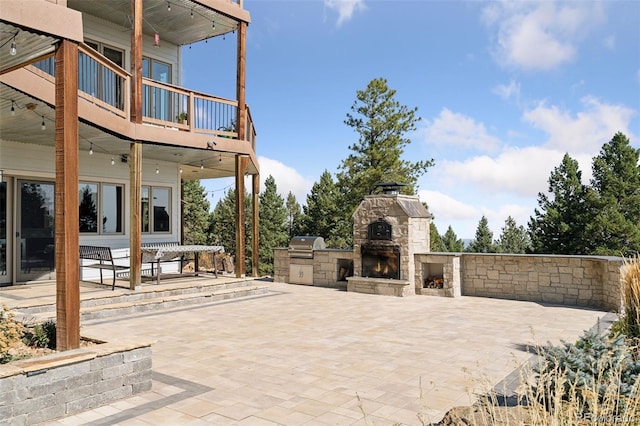 view of patio with an outdoor stone fireplace, a balcony, and area for grilling