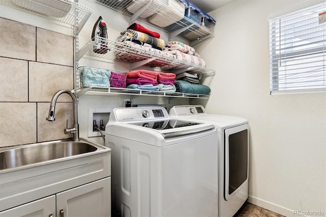 clothes washing area featuring sink, washing machine and dryer, and cabinets