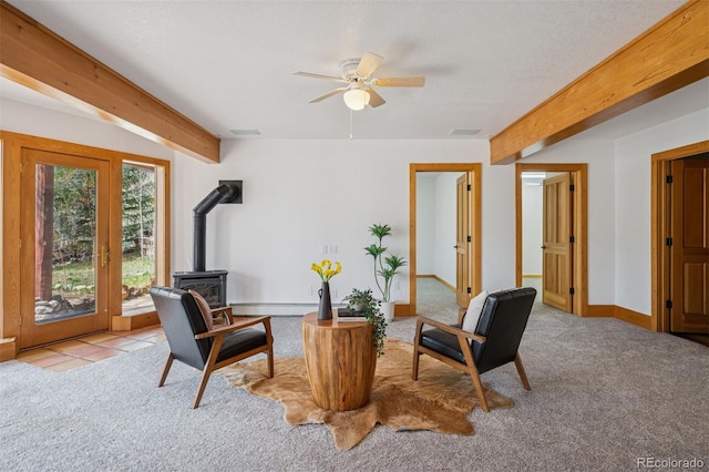sitting room featuring beamed ceiling, carpet, ceiling fan, and a wood stove