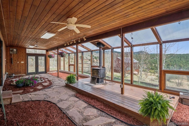 sunroom featuring french doors, track lighting, plenty of natural light, and a wood stove