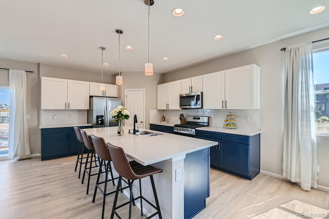 kitchen featuring a center island with sink, hanging light fixtures, sink, blue cabinetry, and appliances with stainless steel finishes