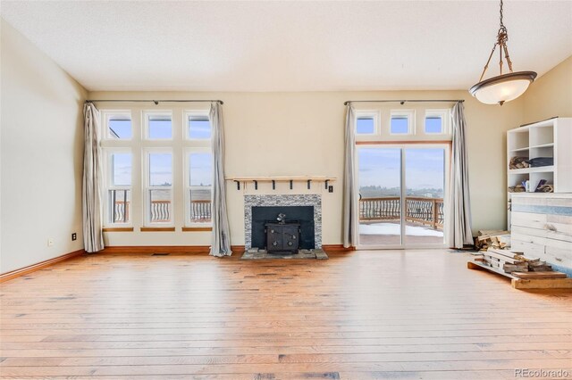 unfurnished living room with a wood stove, visible vents, light wood-style flooring, and baseboards