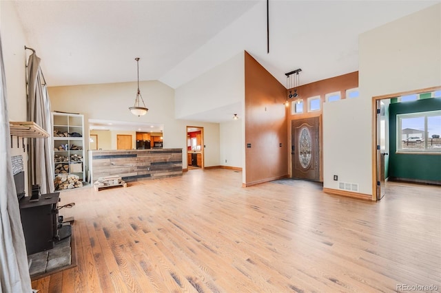 living room featuring visible vents, a wood stove, high vaulted ceiling, light wood-type flooring, and baseboards