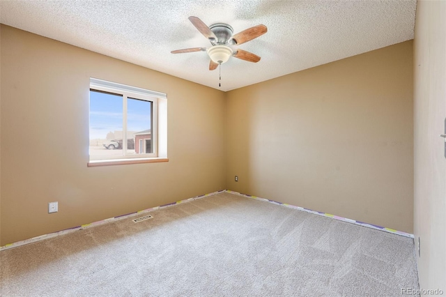 spare room with carpet floors, visible vents, ceiling fan, and a textured ceiling