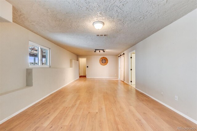 unfurnished room featuring light wood-style floors, visible vents, a textured ceiling, and baseboards