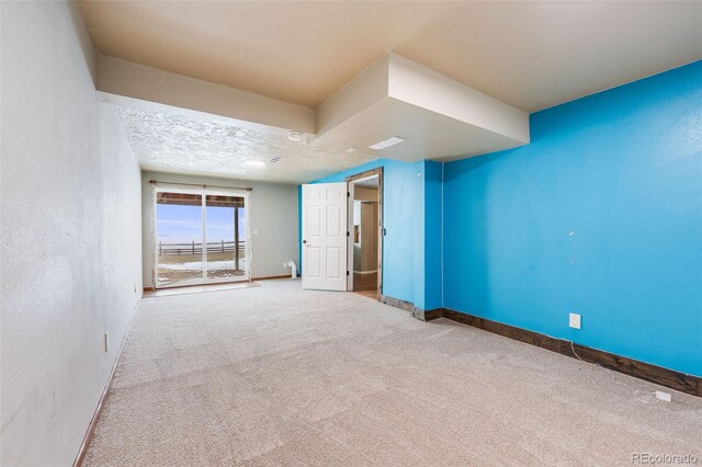 carpeted spare room with a textured ceiling, a textured wall, and baseboards