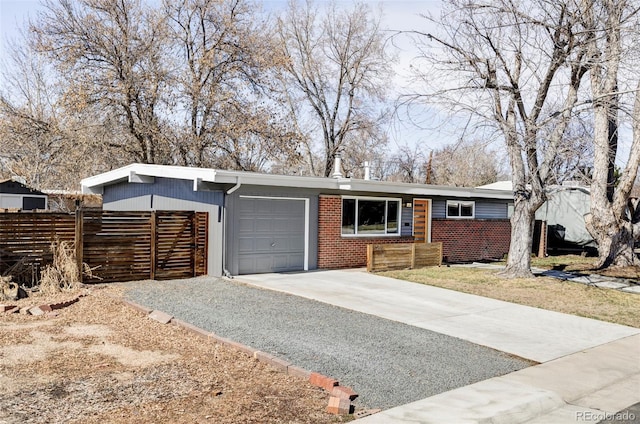 view of front facade with driveway, brick siding, an attached garage, and fence