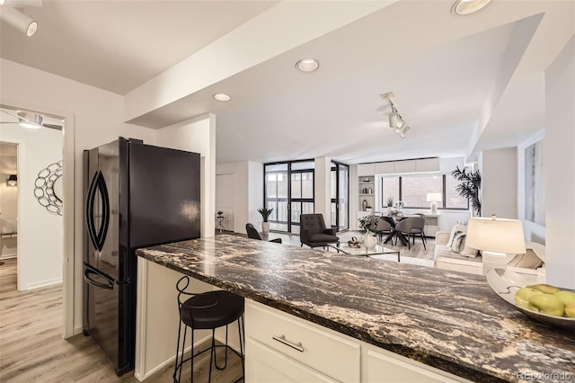 1551 Larimer St Unit 703, Denver, CO 80202 - kitchen featuring freestanding refrigerator, light wood finished floors, dark stone countertops, open floor plan, and white cabinetry
