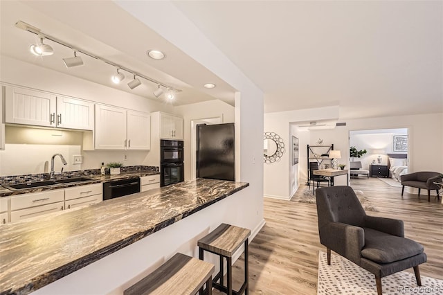 1551 Larimer St Unit 703, Denver, CO 80202 - kitchen featuring black appliances, a sink, light wood-style flooring, white cabinets, and a breakfast bar