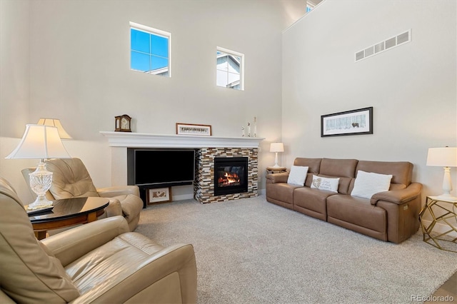 living room with a stone fireplace, a high ceiling, carpet, and visible vents