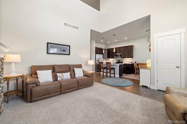 living area with dark wood-style floors, visible vents, and a towering ceiling