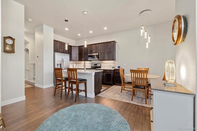 kitchen with arched walkways, appliances with stainless steel finishes, light countertops, dark brown cabinets, and dark wood-style flooring