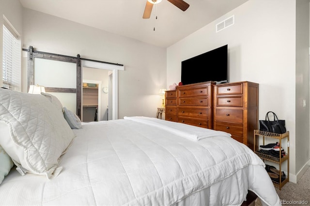 carpeted bedroom featuring visible vents, a walk in closet, ceiling fan, baseboards, and a barn door