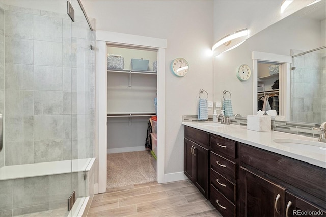 bathroom with double vanity, a shower stall, a spacious closet, and a sink