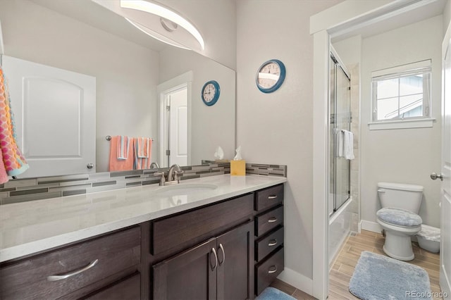 bathroom featuring vanity, wood finished floors, baseboards, shower / bath combination with glass door, and toilet