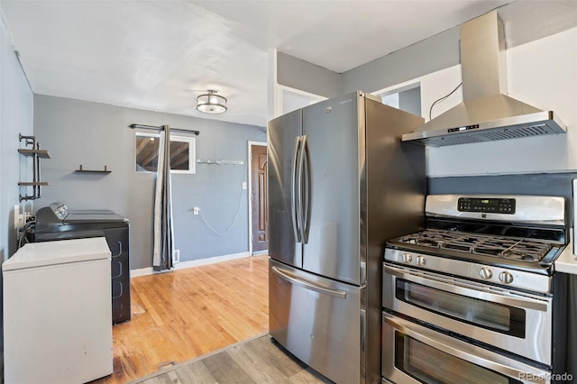 kitchen with washing machine and clothes dryer, light wood-type flooring, appliances with stainless steel finishes, and wall chimney exhaust hood