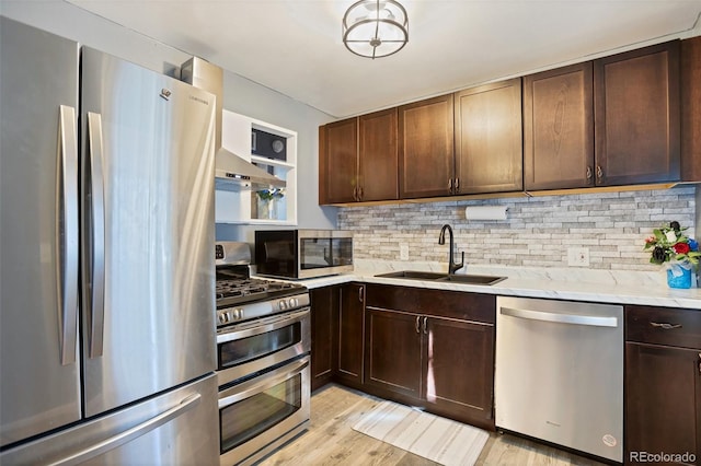 kitchen with appliances with stainless steel finishes, decorative backsplash, light hardwood / wood-style floors, light stone countertops, and sink