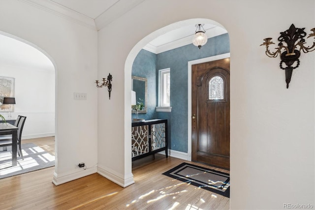 foyer featuring baseboards, crown molding, arched walkways, and wood finished floors