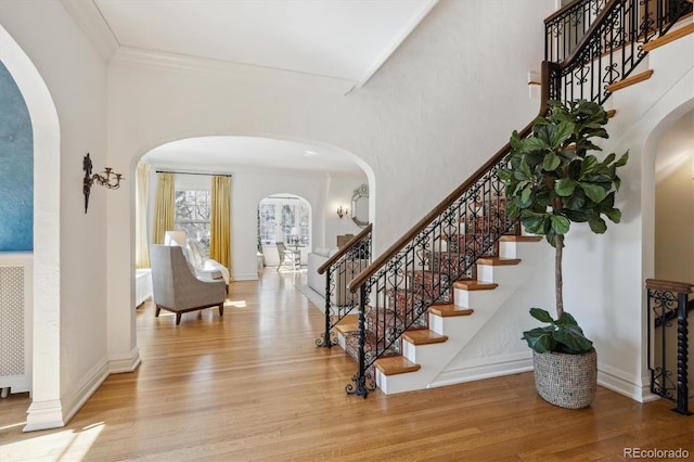 foyer with ornamental molding, arched walkways, baseboards, and wood finished floors