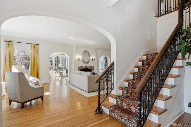 interior space featuring arched walkways, a fireplace, baseboards, and wood finished floors