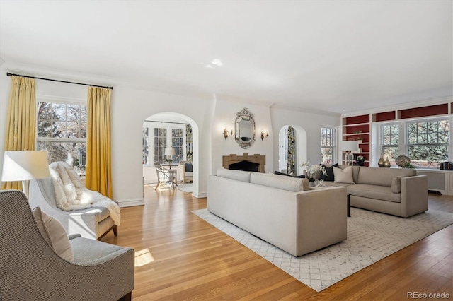 living area with arched walkways, a fireplace, wood finished floors, baseboards, and crown molding