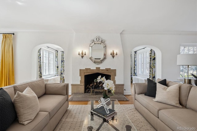 living area with light wood finished floors, arched walkways, a fireplace with raised hearth, and crown molding