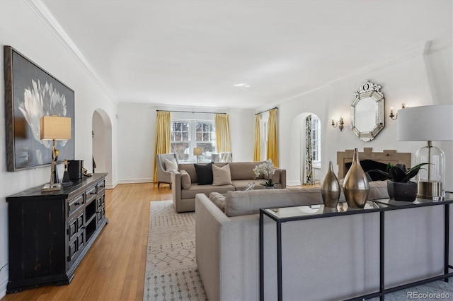 living area featuring arched walkways, baseboards, wood finished floors, and crown molding