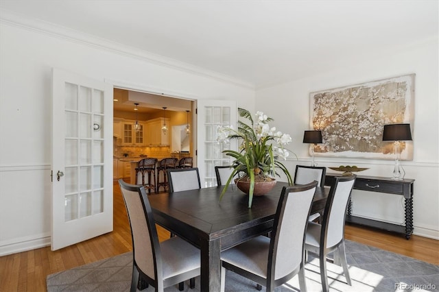 dining room with french doors, ornamental molding, wood finished floors, and baseboards